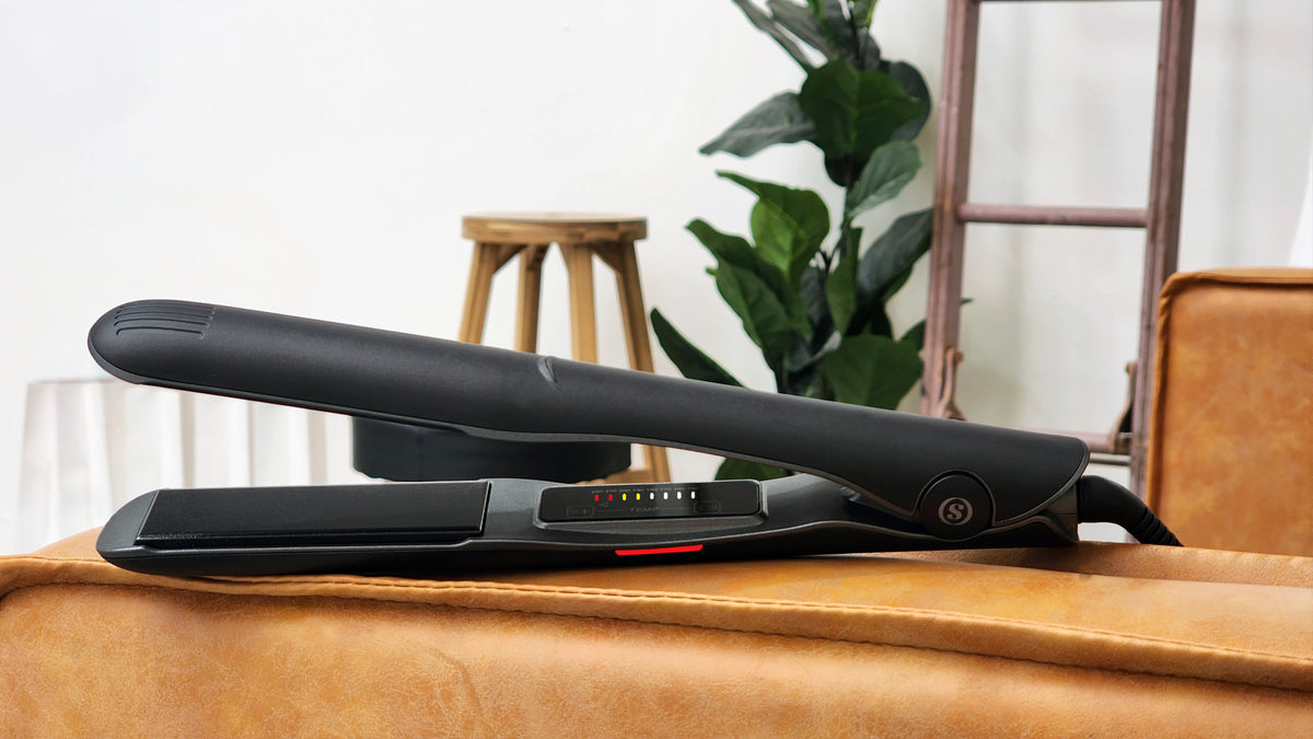 An open black Omnia styler on a tan chair, with its controls and red side indicator visible.