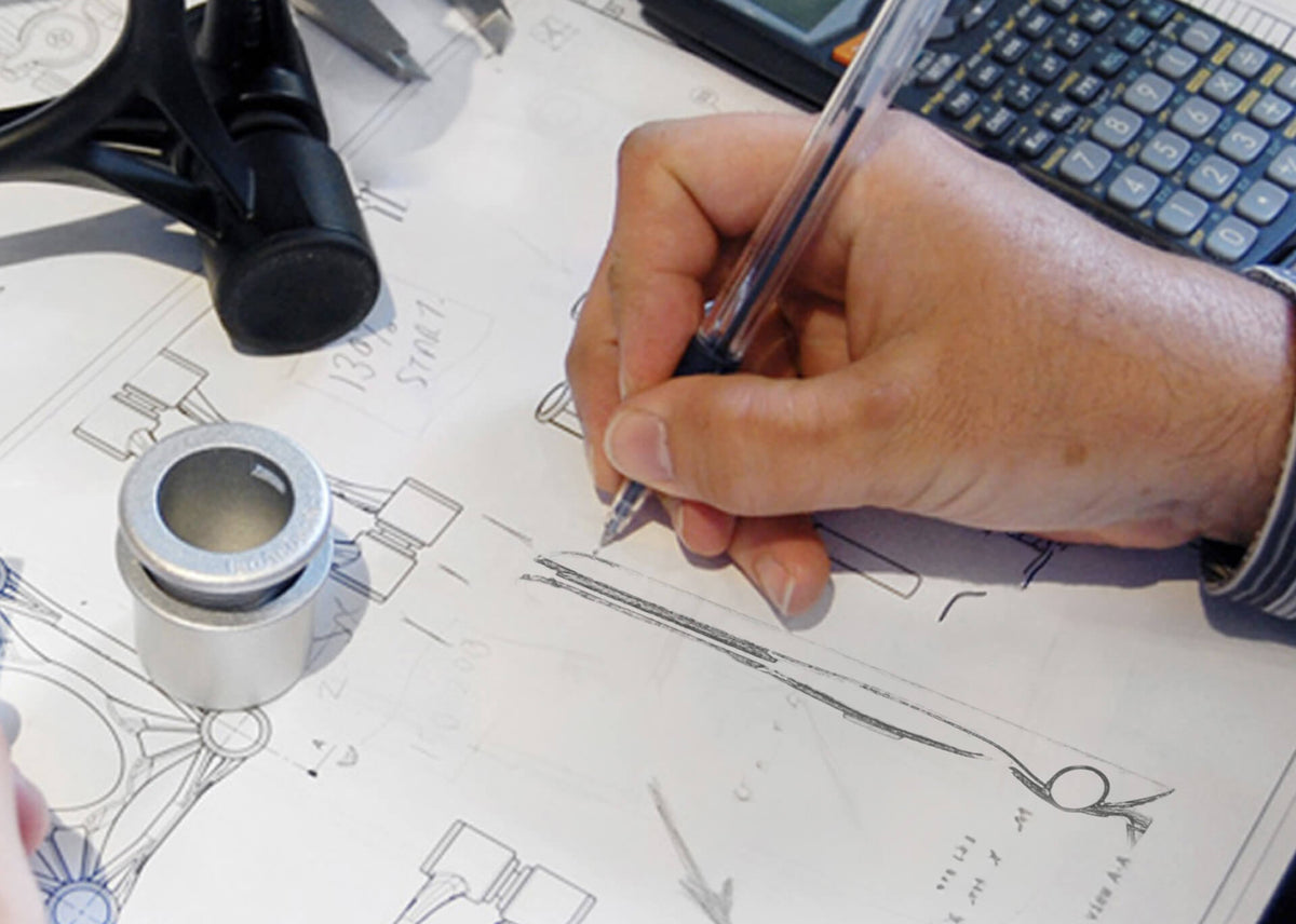 A hand sketching product-design drawings beside components and a calculator.