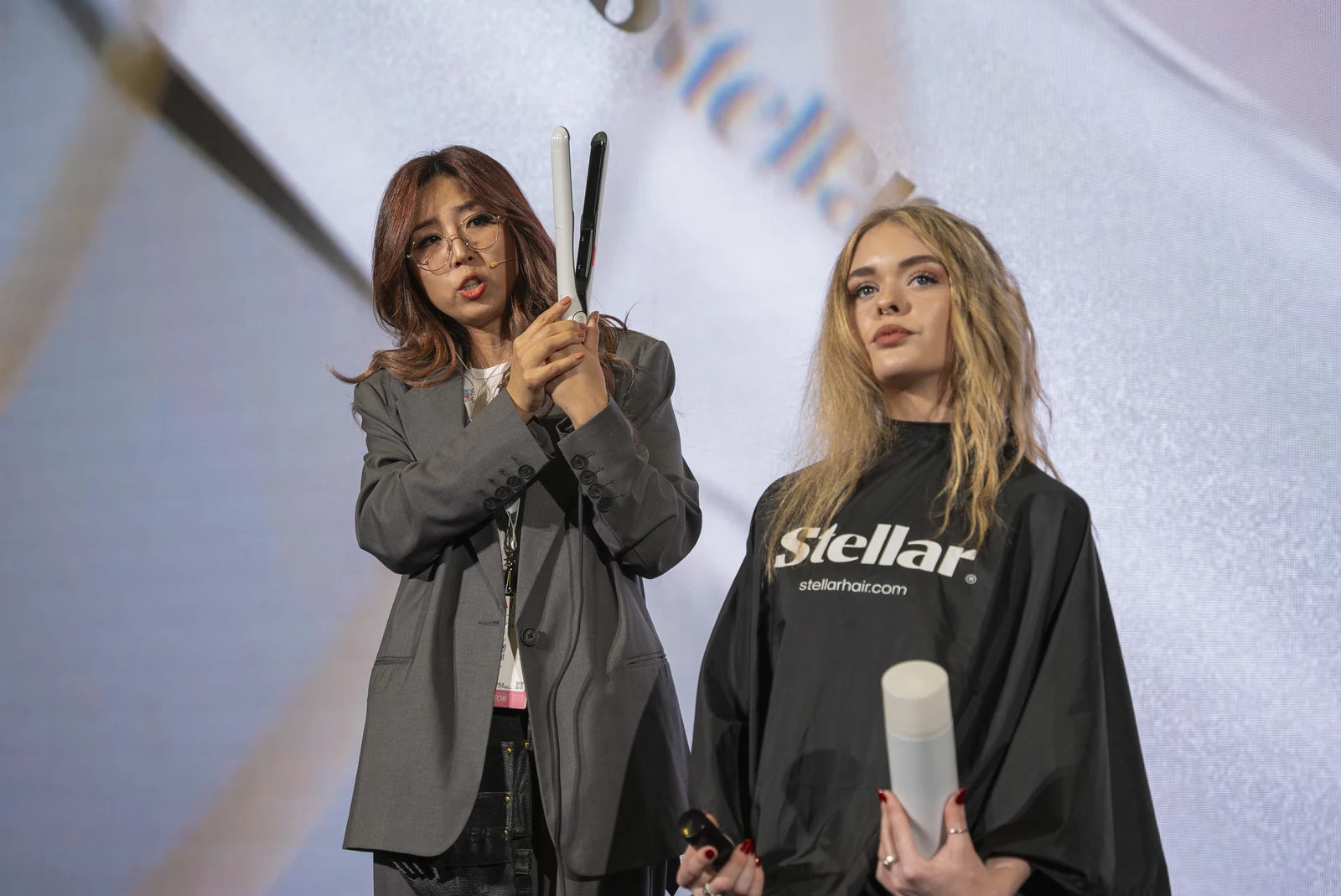 A styling educator demonstrating a white Omnia styler beside a seated model.